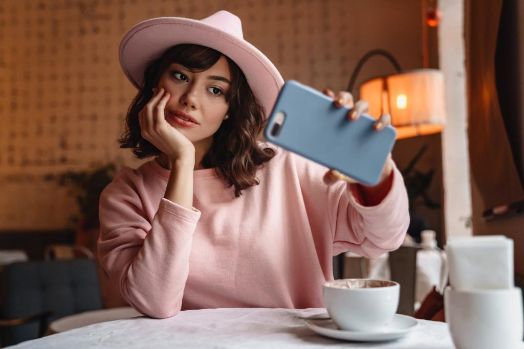 Woman indoors in cafe using mobile phone take a selfie.